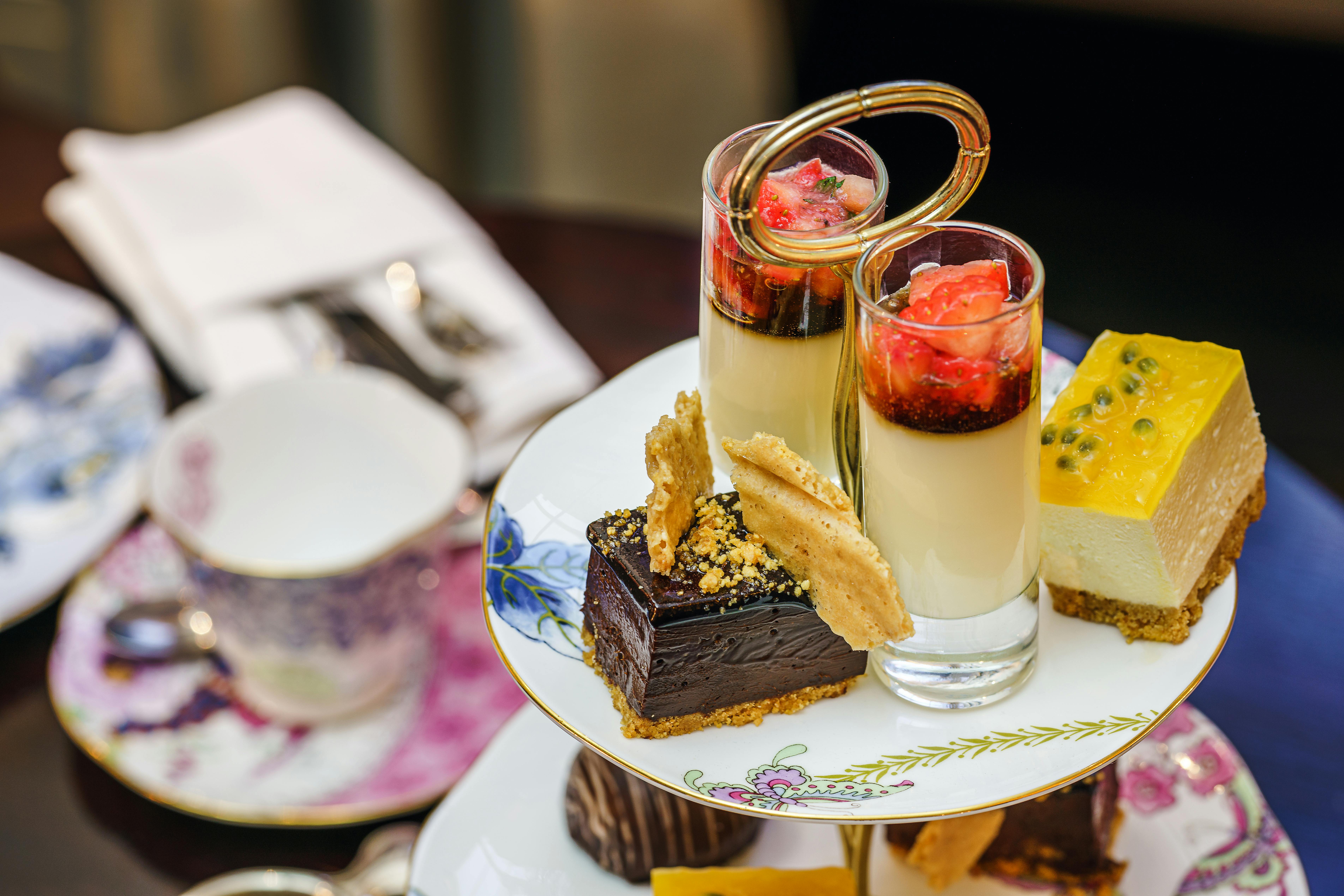 Vegan high tea: feestje met stijl Luxe high tea etagère met chocoladetaart, panna cotta met aardbeien en passievruchtencheesecake op sierlijk porselein